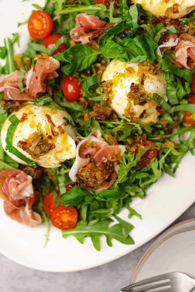 closeup shot of arugula with prosciutto and burrata and tomatoes drizzled with balsamic