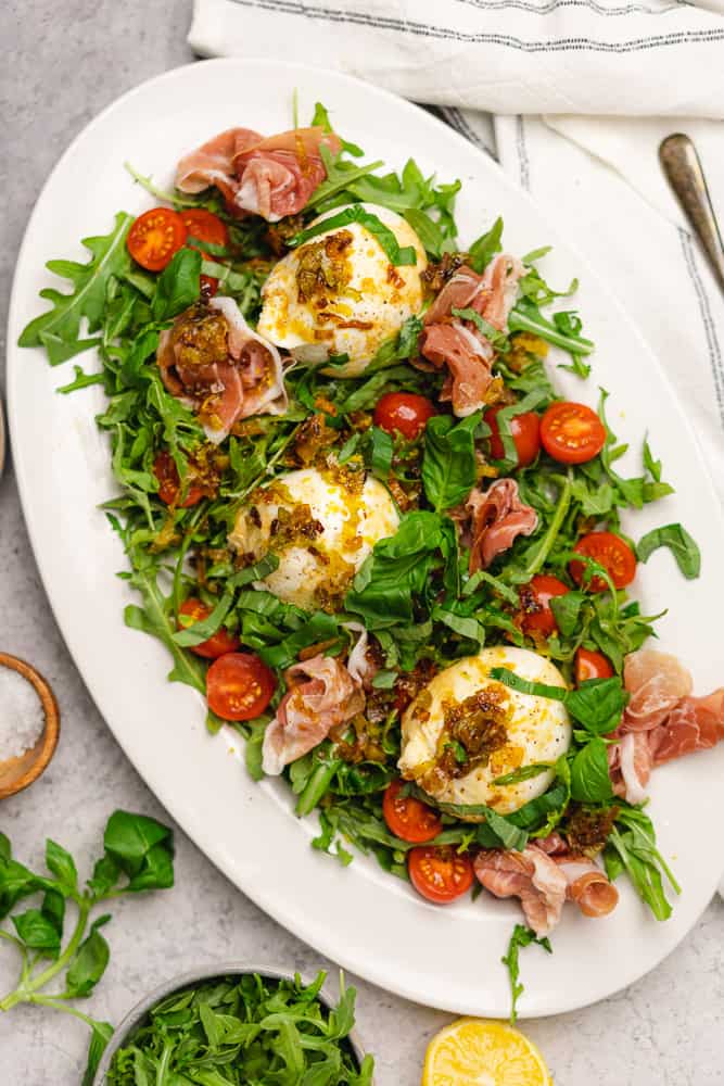 fresh Burrata and Prosciutto salad with tomatoes, fried leeks and balsamic vinegar on a bed of arugula