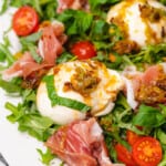 closeup shot of a ball of burrata with prosciutto tomatoes basil and arugula