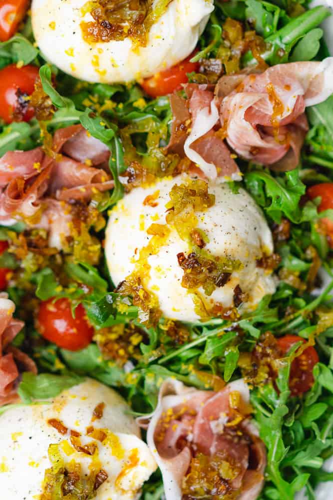 closeup shot of burrata and prosciutto salad on a bed of arugula with tomatoes