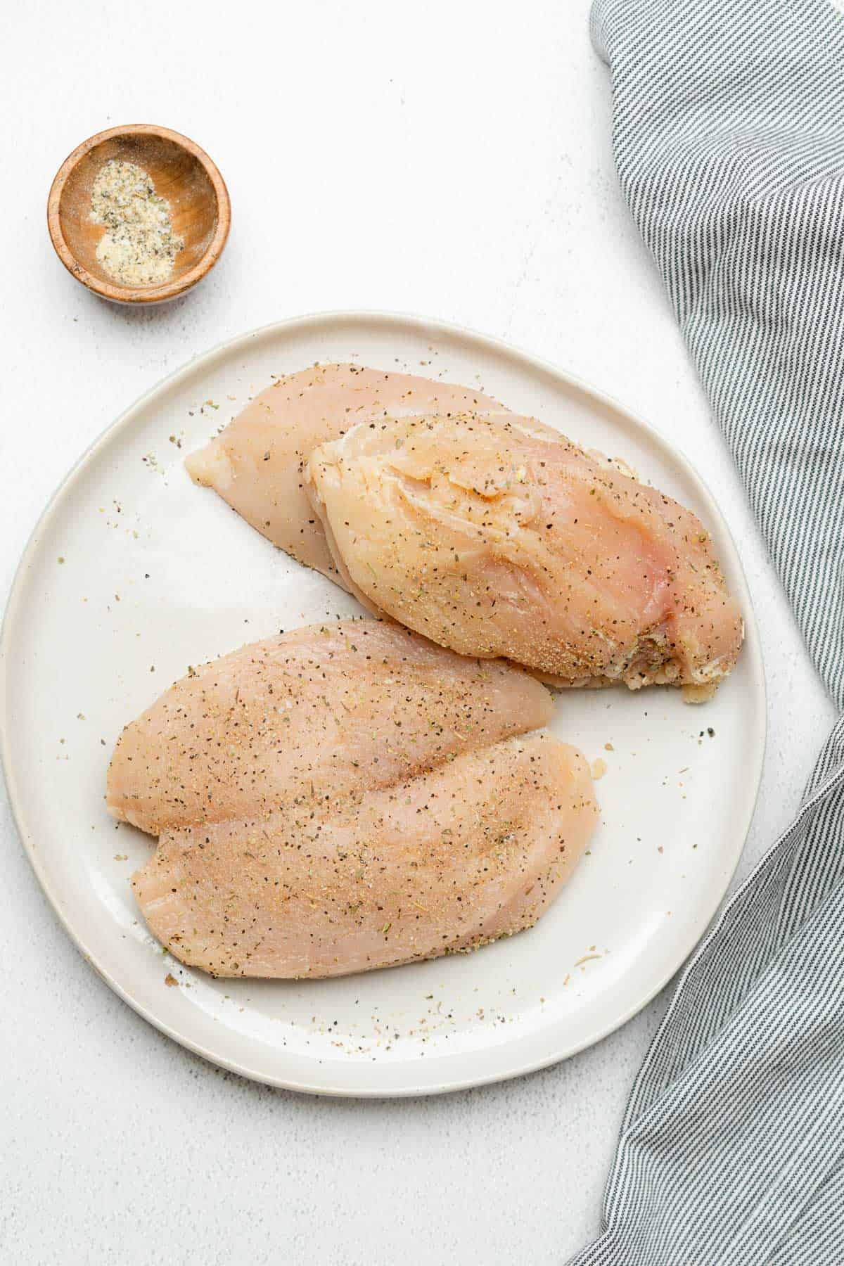 raw chicken breasts cut open on a plate seasoned with plenty of seasoning 