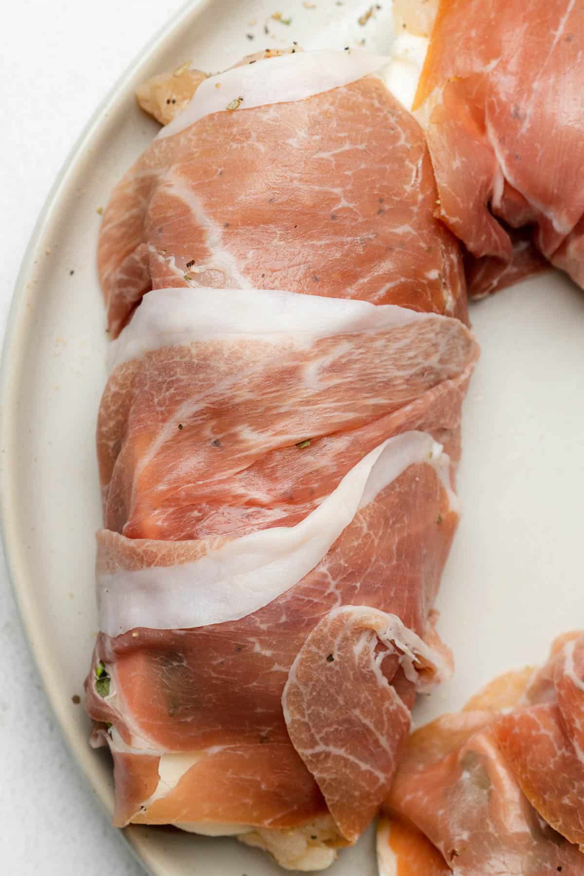 raw chicken wrapped in prosciutto on a plate 
