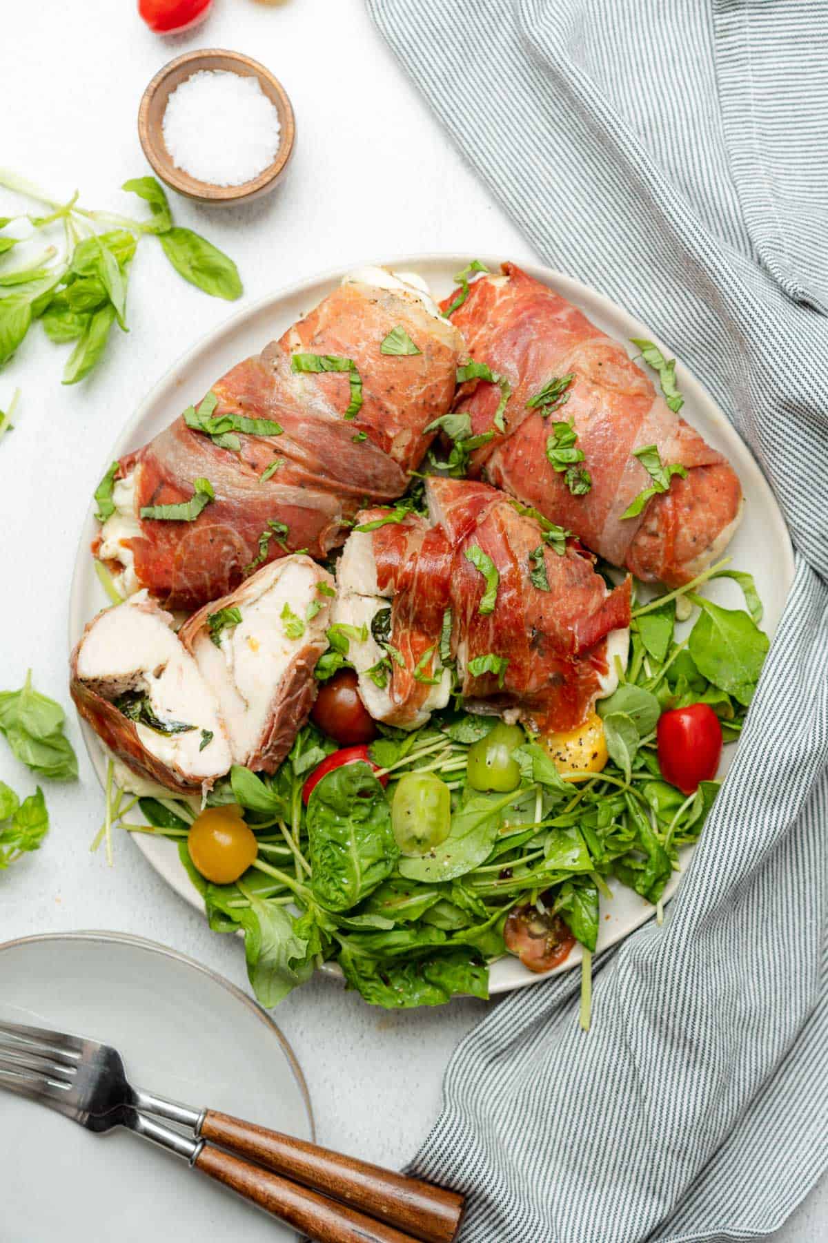 plate with bright arugula salad with tomatoes and chicken wrapped in parma ham with mozzarella cheese
