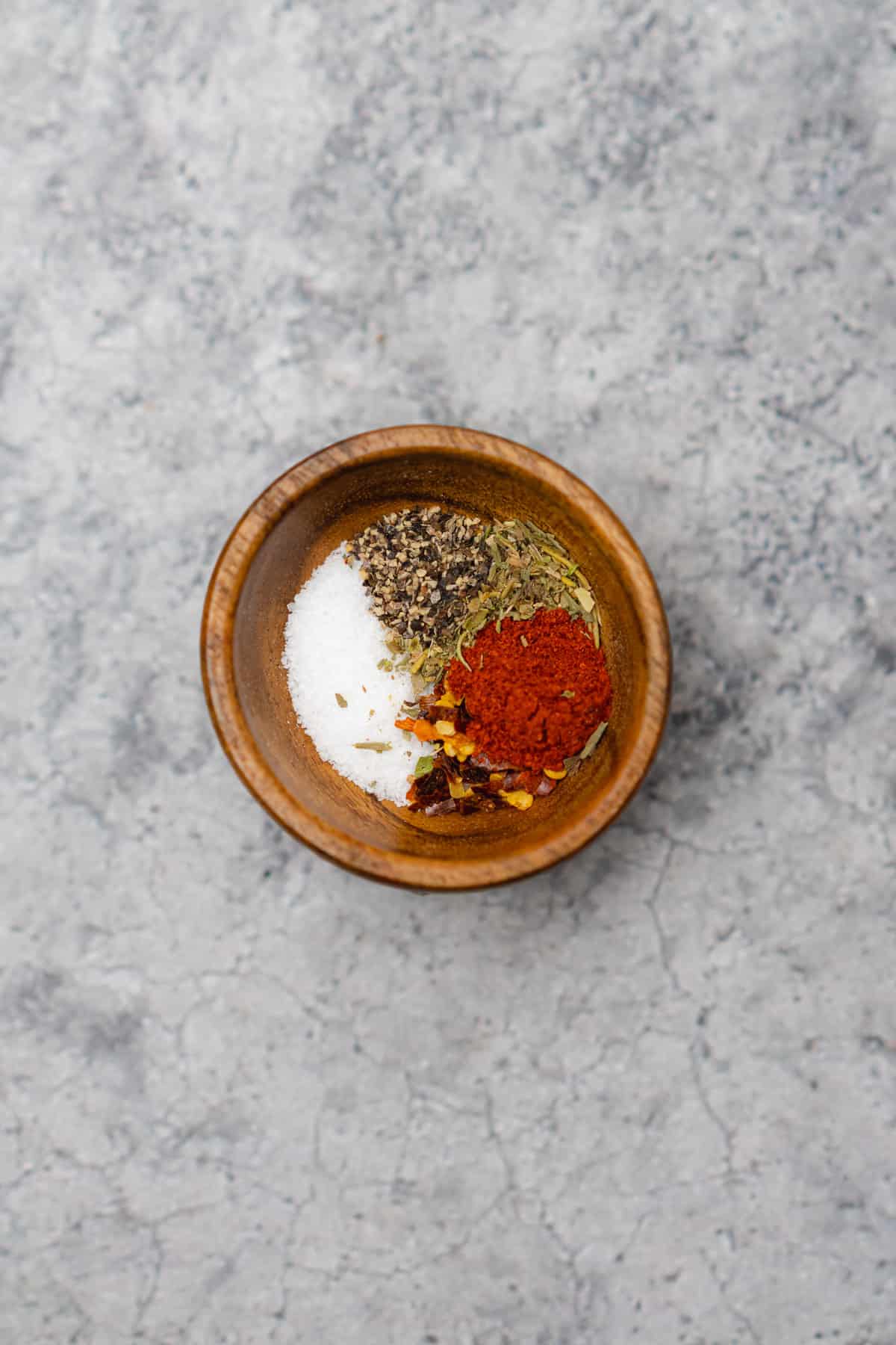 seasonings with salt pepper red pepper flakes italian seasonings and smoked paprika in a small wood dish