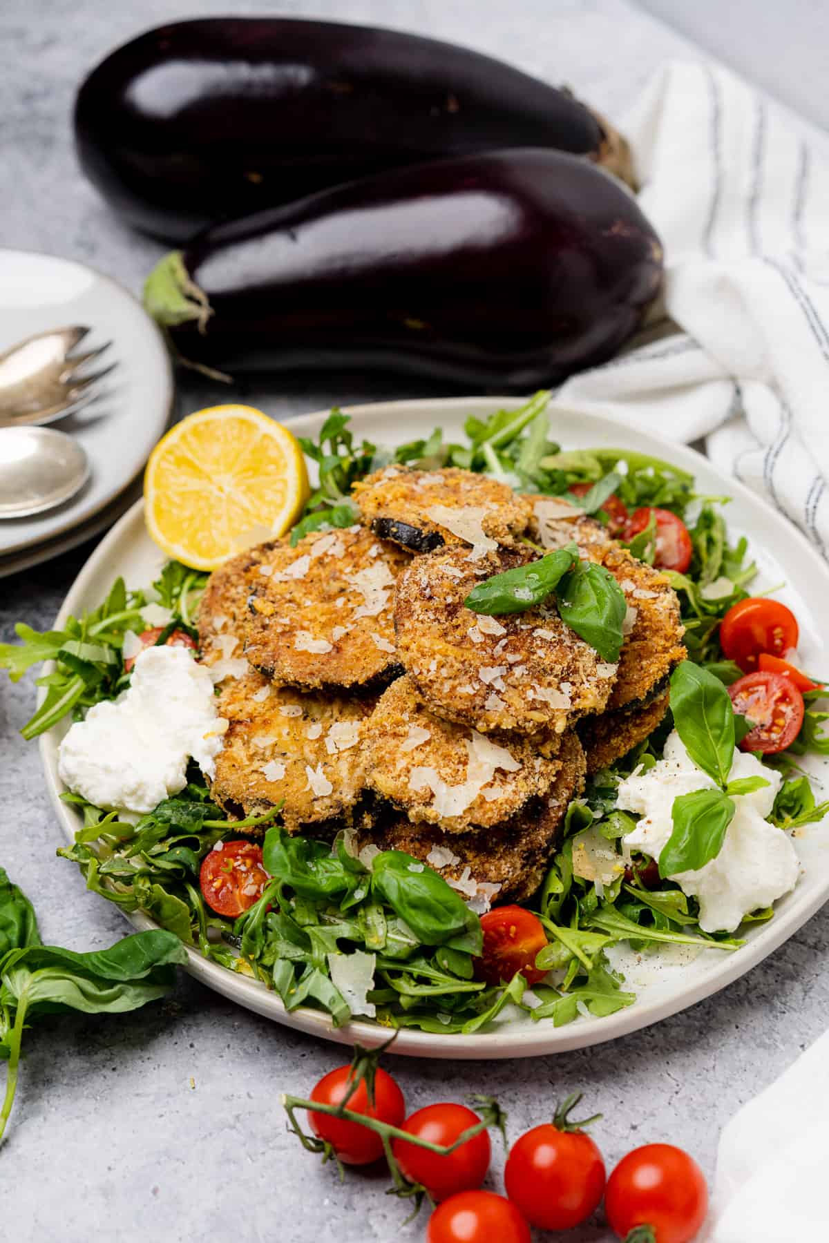eggplant milanese on a white plate with arugula salad ricotta lemon and tomatoes