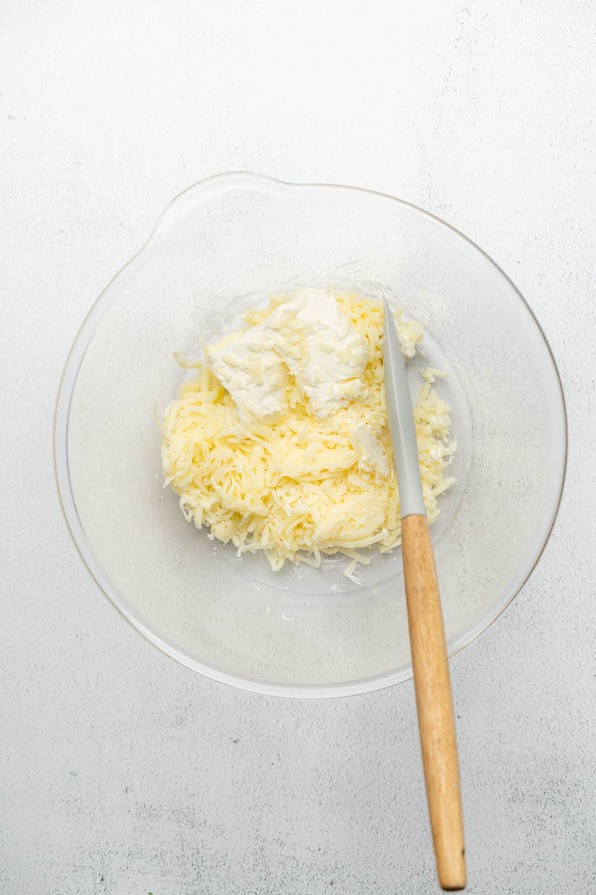 mozzarella cheese and cream cheese in a glass bowl with a rubber spatula 