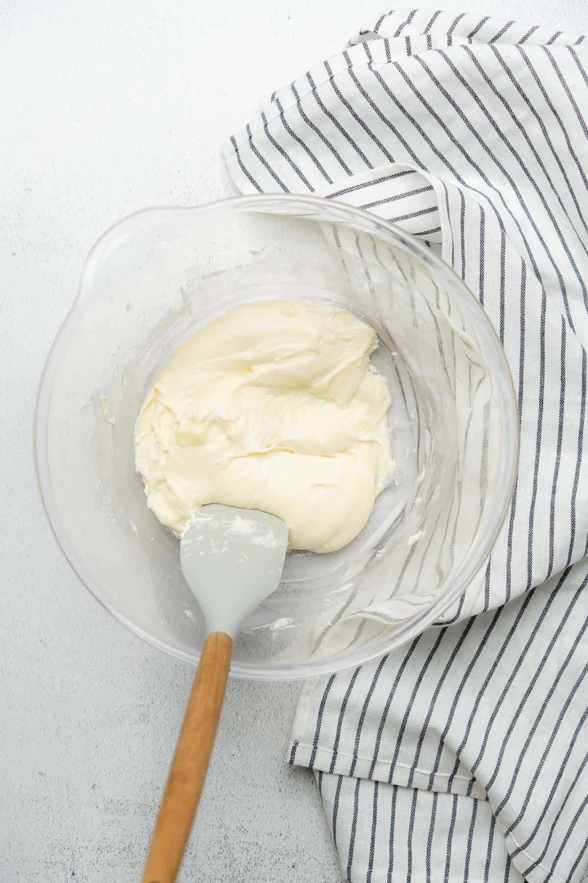 melted cream cheese and mozzarella cheese in a glass bowl with a rubber spatula and napkins 