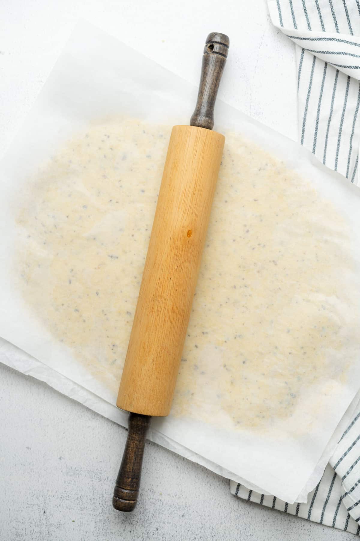 rolling keto fat head dough between two pieces of parchment paper with a rolling pin 