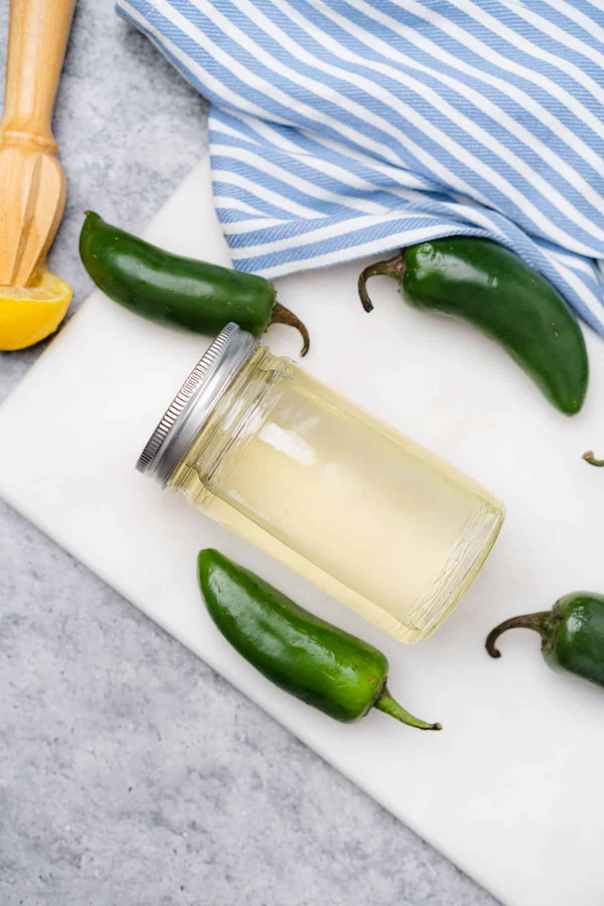 jalapeno simple syrup in a glass bottle surrounded by fresh jalapenos 