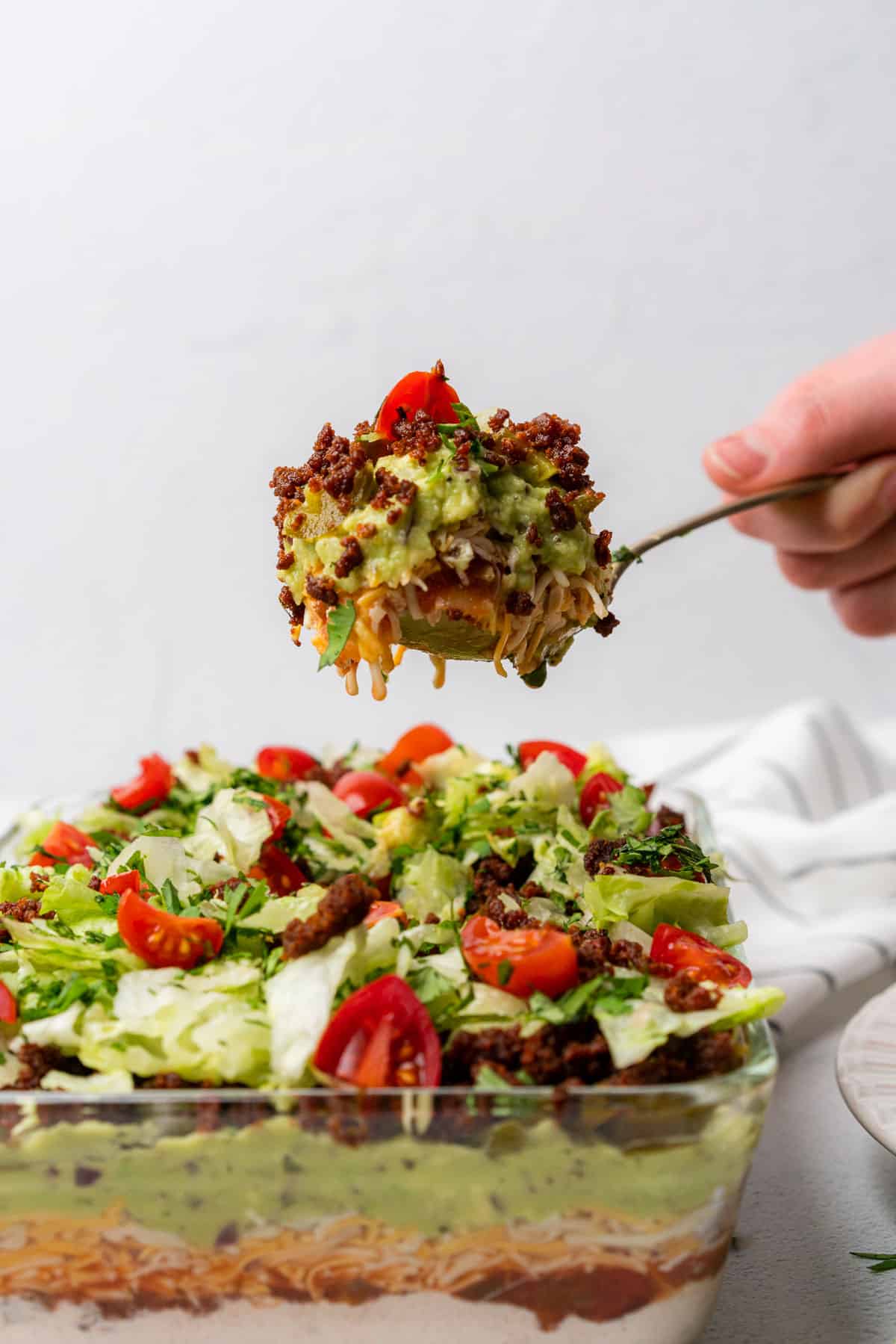 straight on shot of keto 7 layer dip with chorizo cilantro and tomatoes on a spoonful being hand held