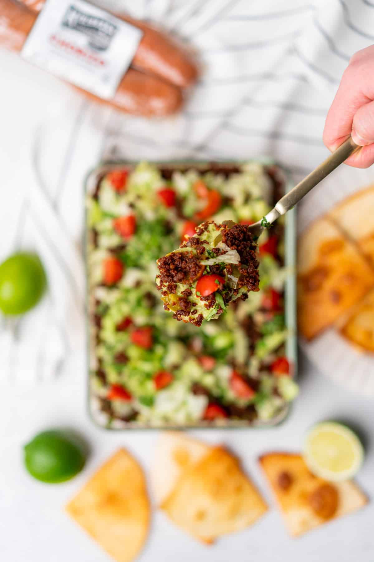 handheld spoonful of keto 7 layer dip with chorizo and limes