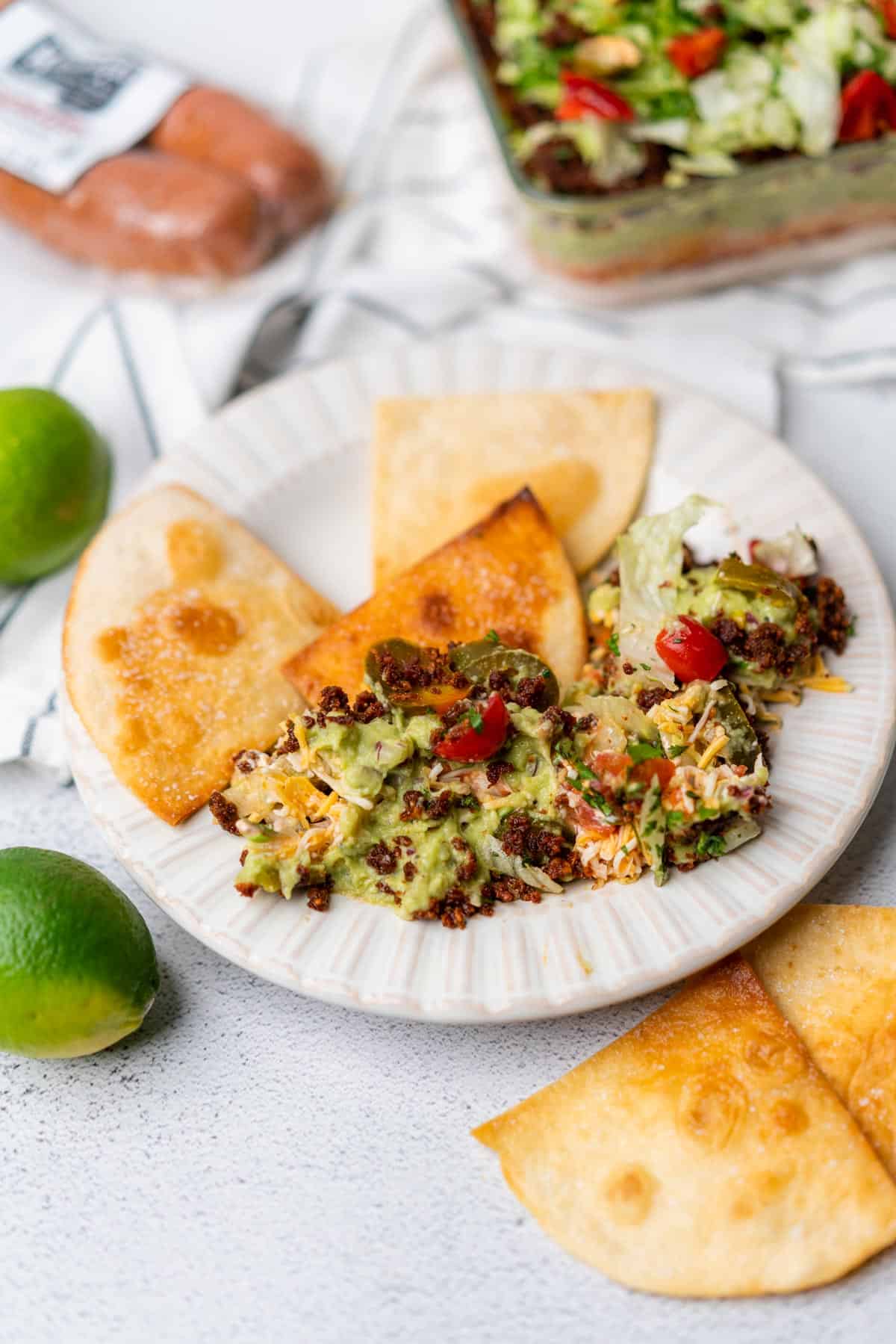 keto 7 layer dip with chorizo limes on a plate with low carb tortilla chips