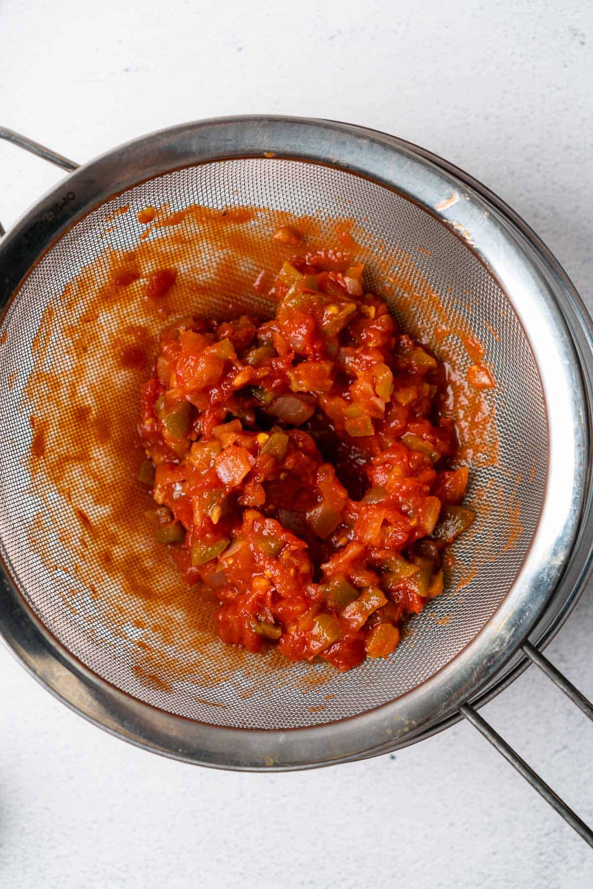 chunky salsa being strained through a metal sieve