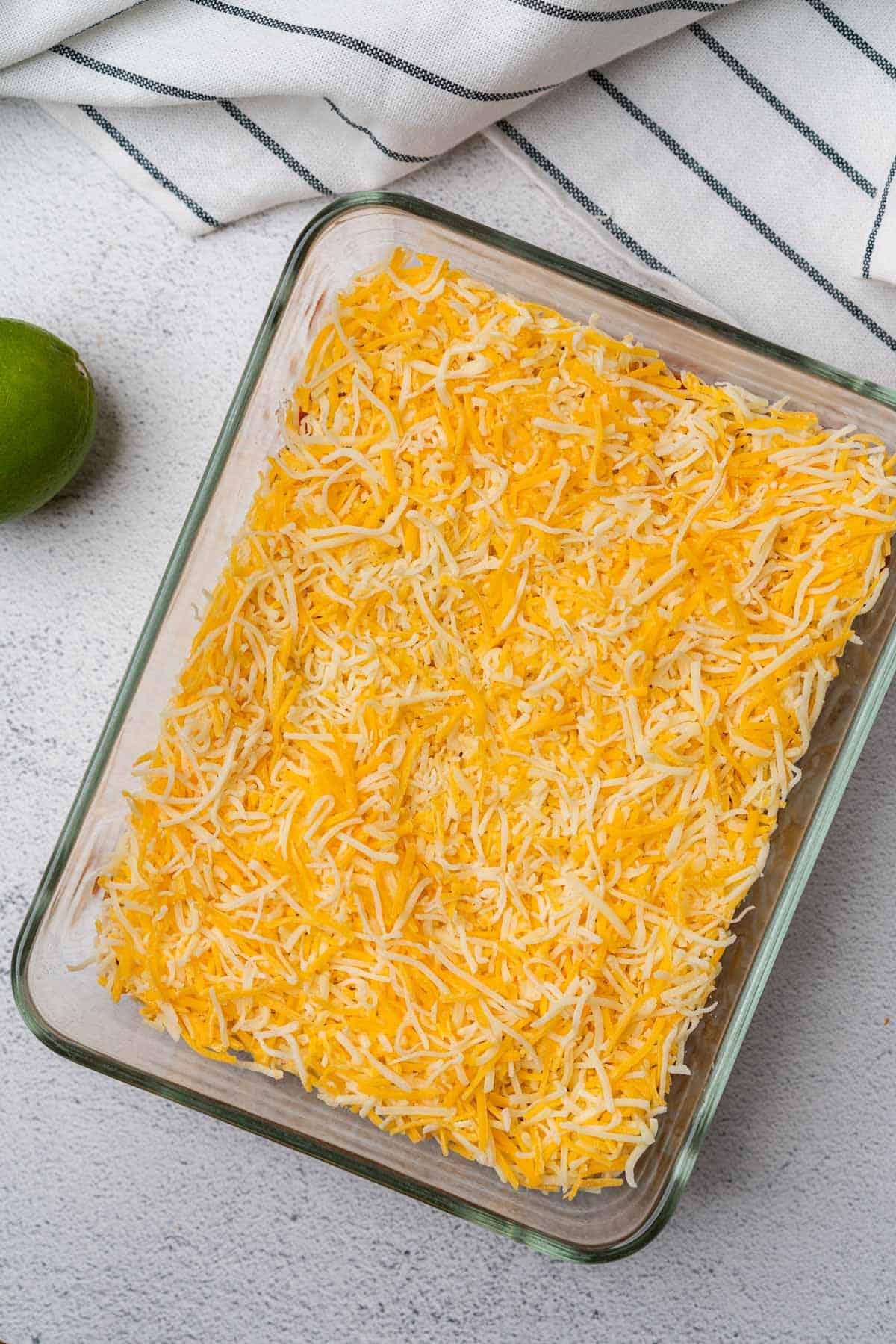 shredded cheese in a glass casserole dish with limes
