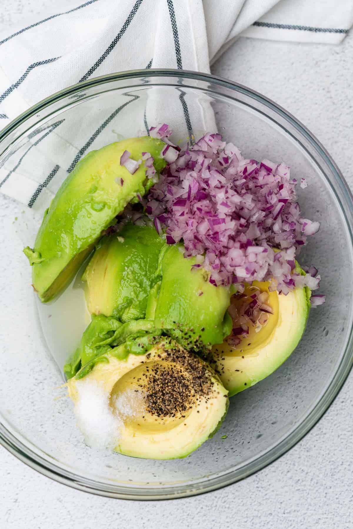 avocados in a bowl with red onion salt pepper and lime juice