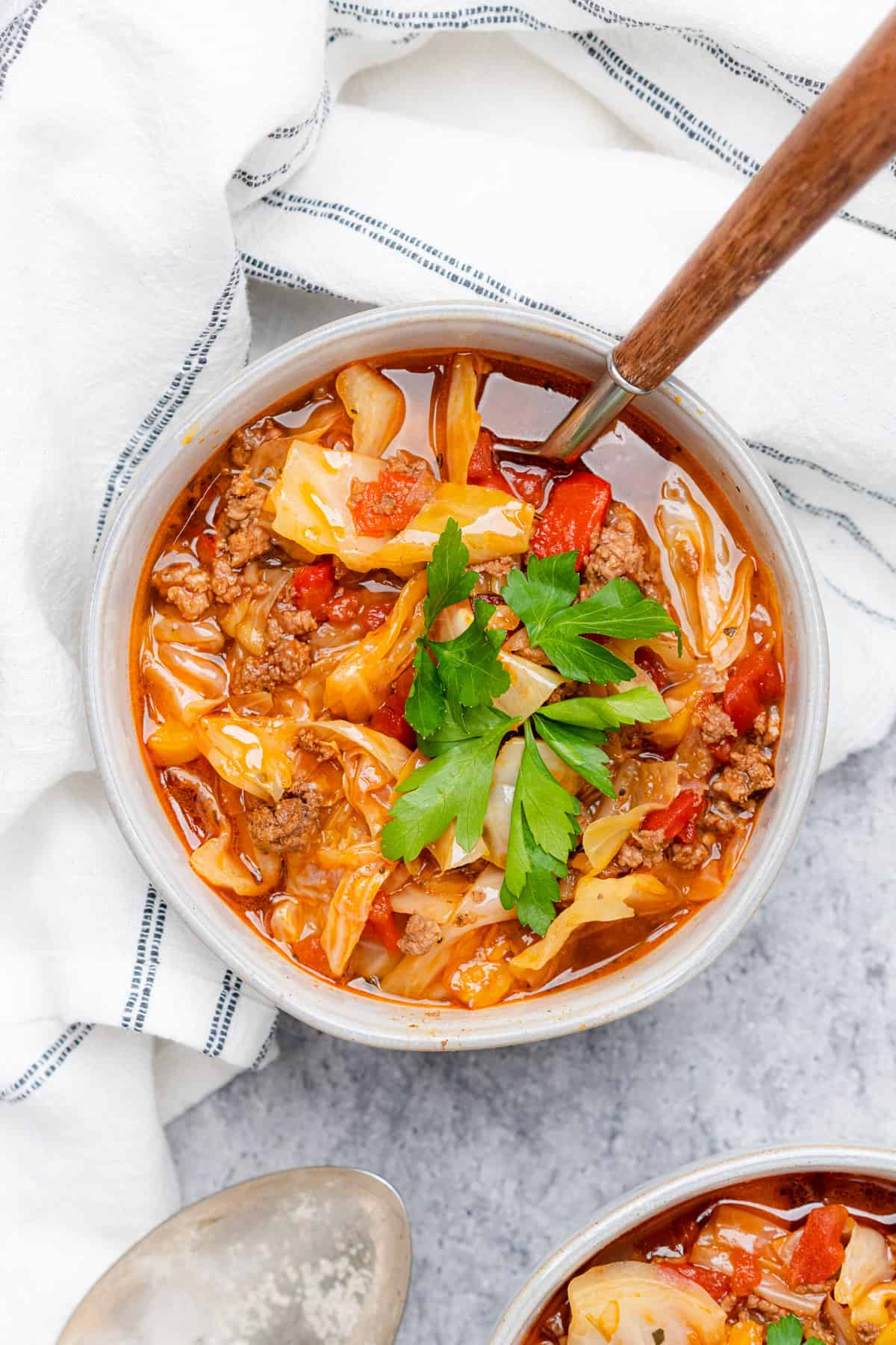 beautiful bowl of keto cabbage roll soup with a wooden spoon white bowl and grey backdrop
