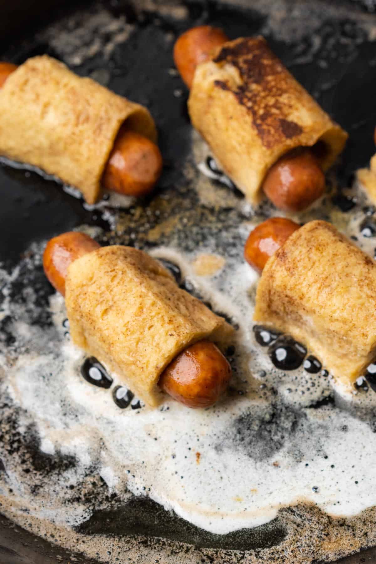 keto french toast pigs in a blanket with egg mixture in a hot skillet with butter