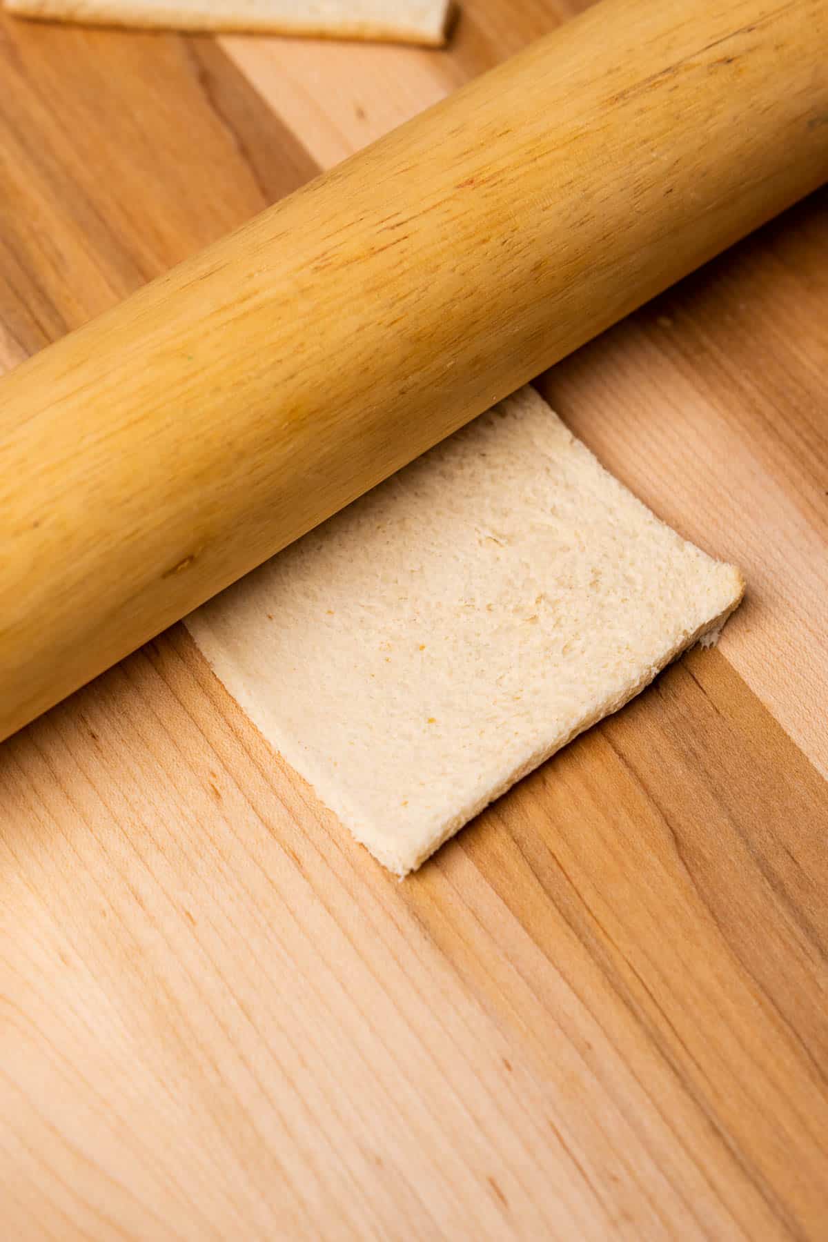 using a rolling pin to flatten a piece of white bread on a cutting board