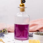glass bottle with a gold handle filled with a bright purple lavender simple syrup