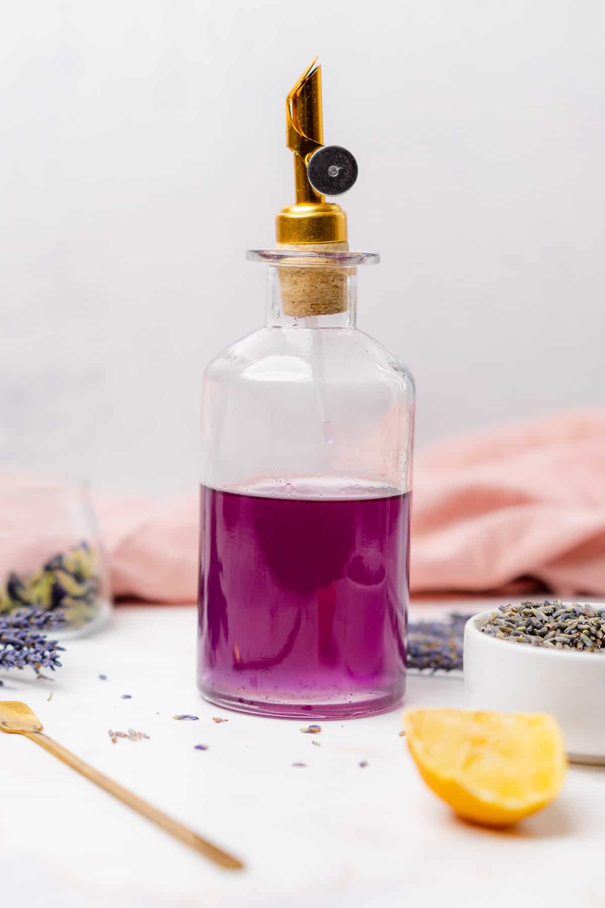 glass bottle with a gold handle filled with a bright purple lavender simple syrup