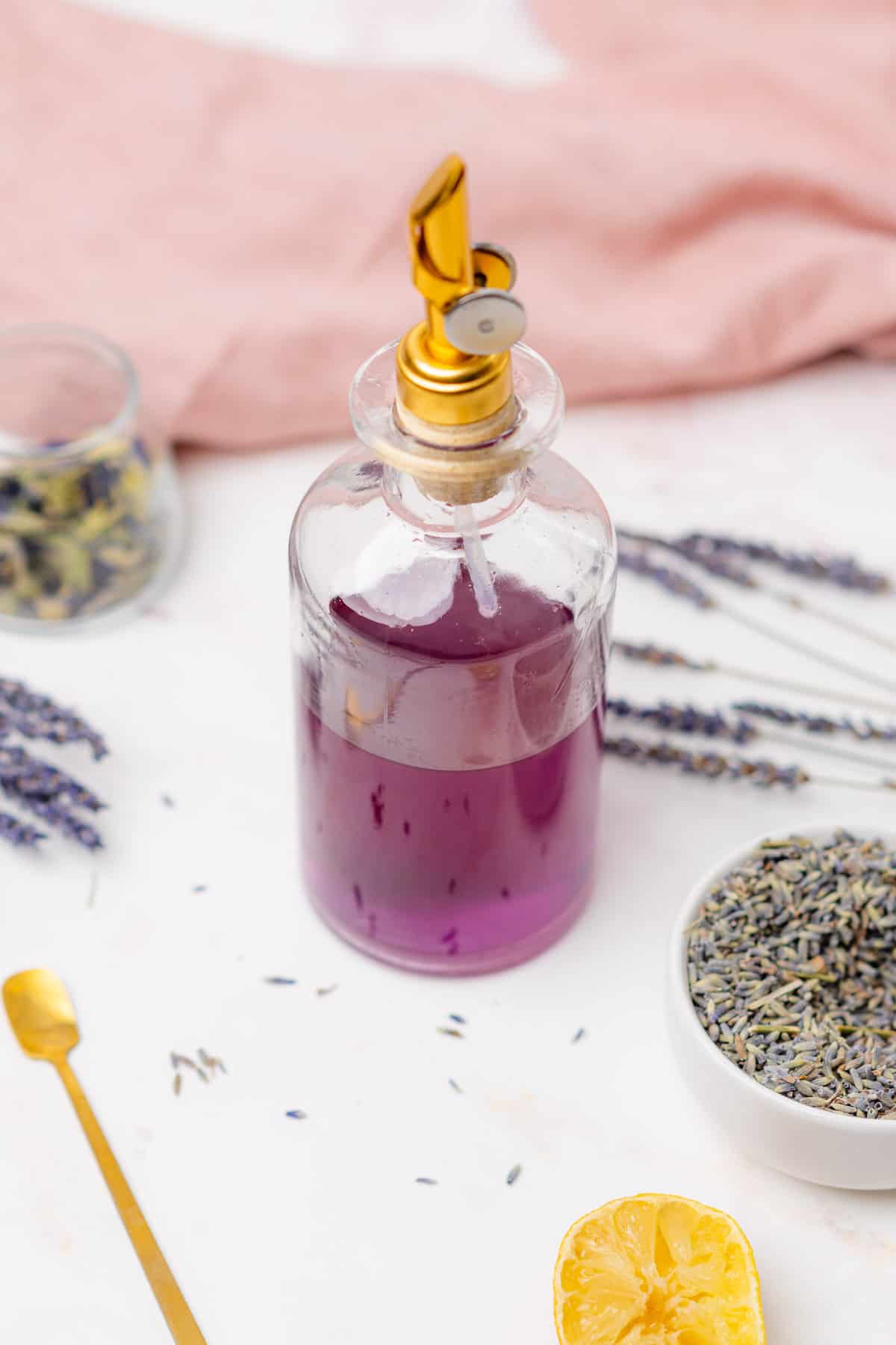 glass bottle with bright purple lavender simple syrup surrounded by lavender buds