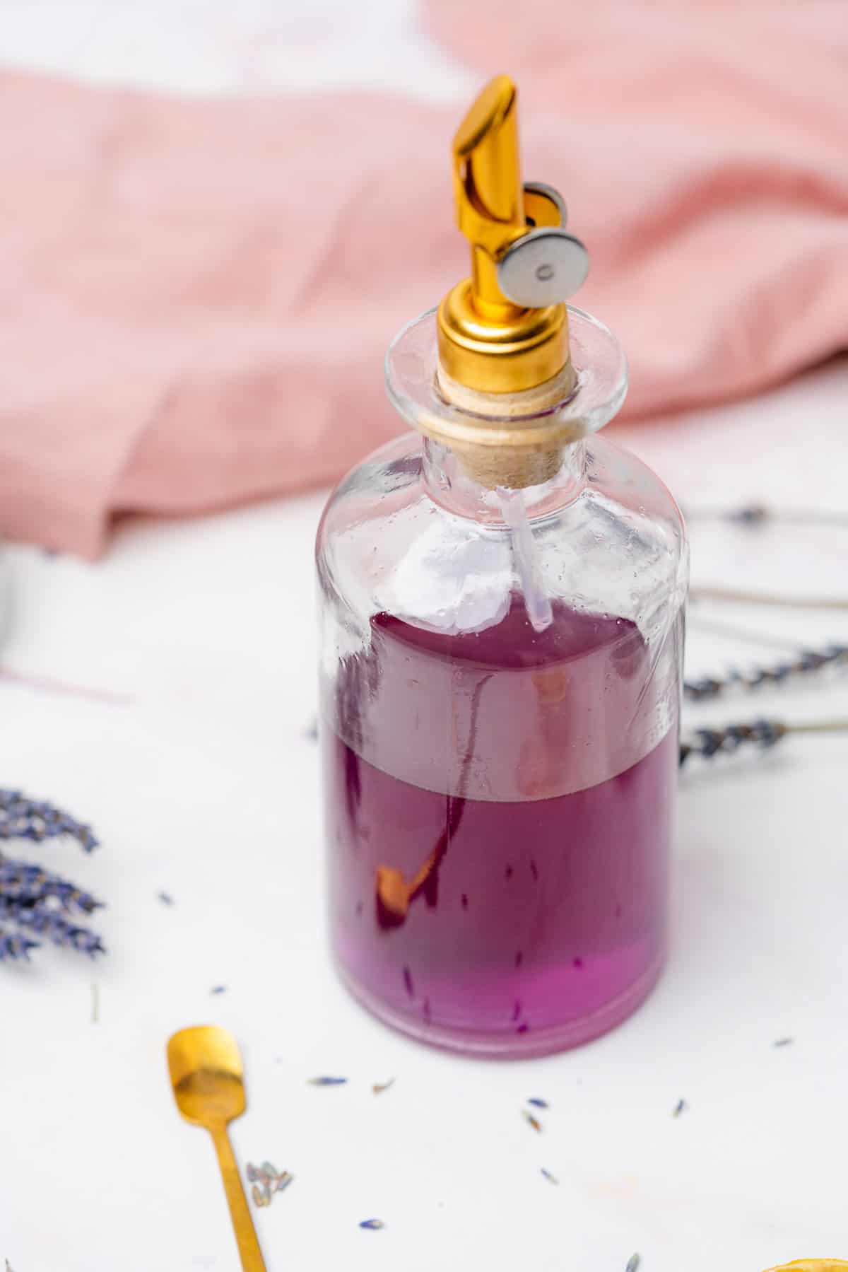 bright purple lavender simple syrup in a glass bottle with a gold pour spout