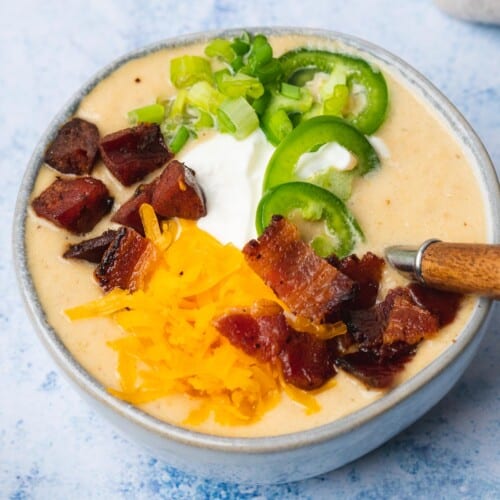 low carb potato soup with bacon jalapenos smoked sausage cheese and sour cream on a blue backdrop