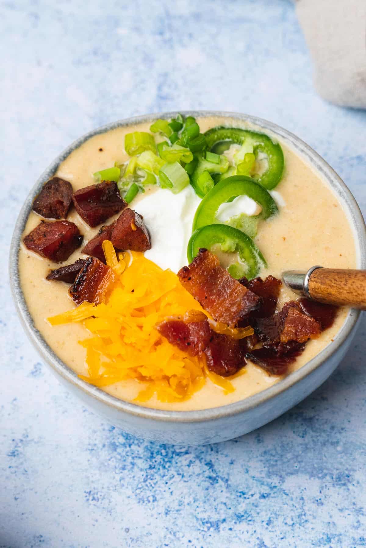 low carb potato soup with bacon jalapenos smoked sausage cheese and sour cream on a blue backdrop