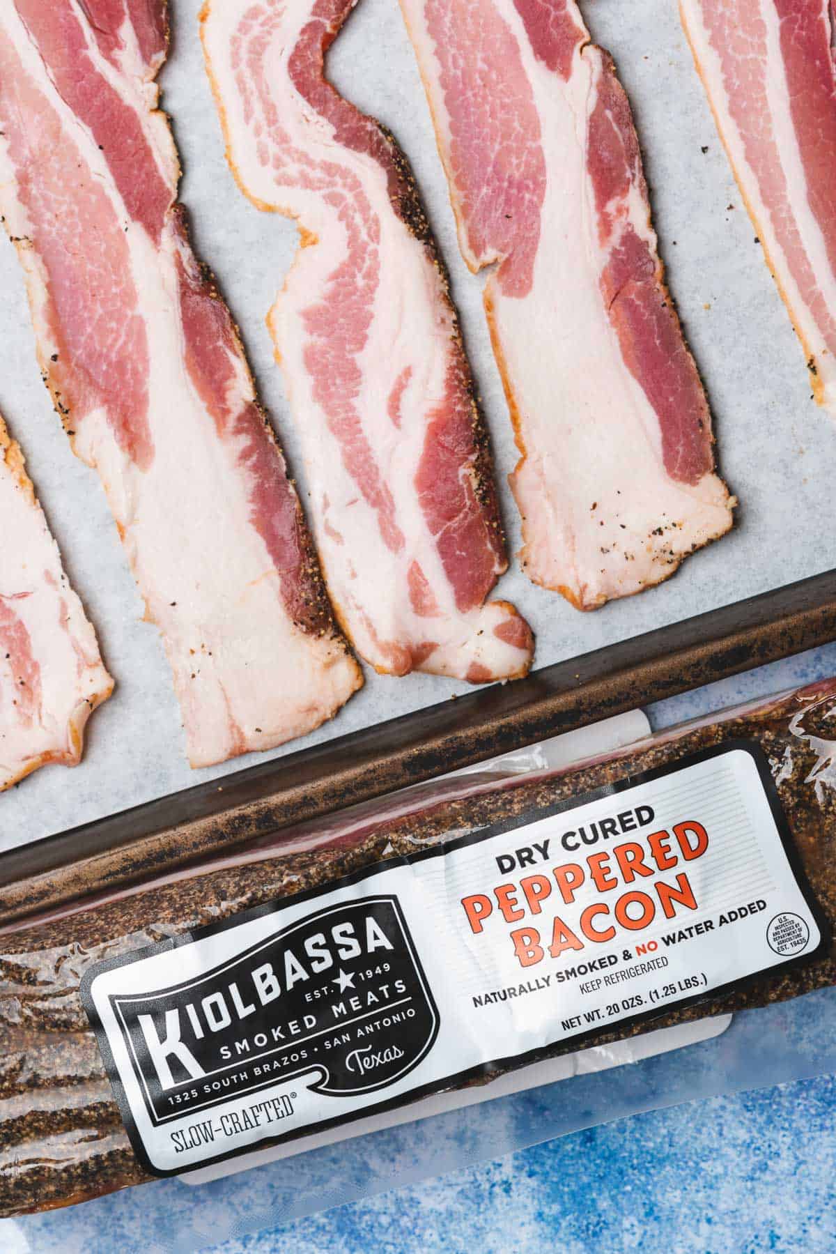 raw kiolbassa smoked meats raw bacon on a baking sheet with a package of kiolbassa smoked meats bacon