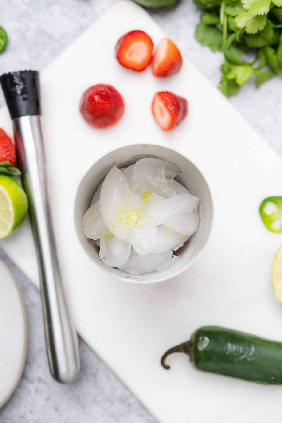 kosher salt and lime zest in a cocktail shaker with ice surrounded by strawberries 