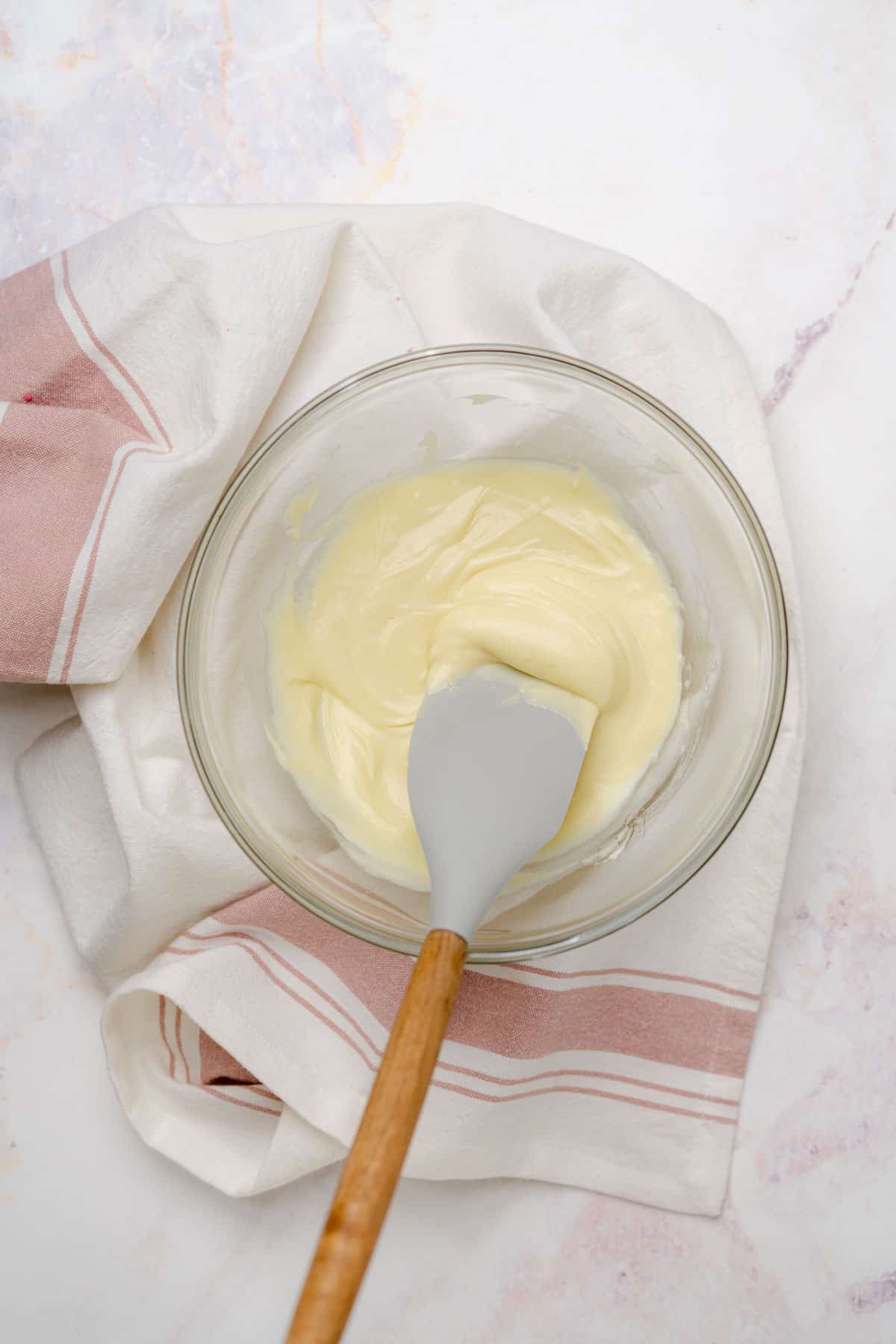 melted white chocolate chips in a glass bowl being stirred with a rubber spatula