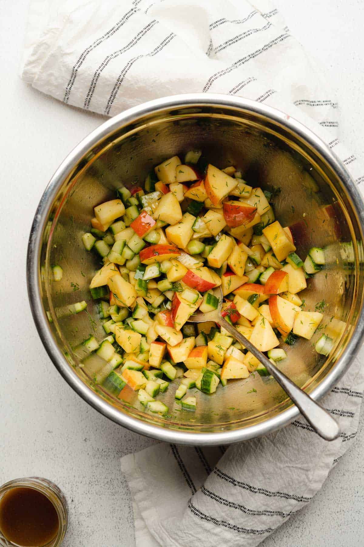 mixing up apple and cucumber salad in a mixing bowl with creamy balsamic dressing 