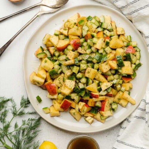 apple and cucumber salad on a white plate with lemon, fresh dill and creamy balsamic vinegar