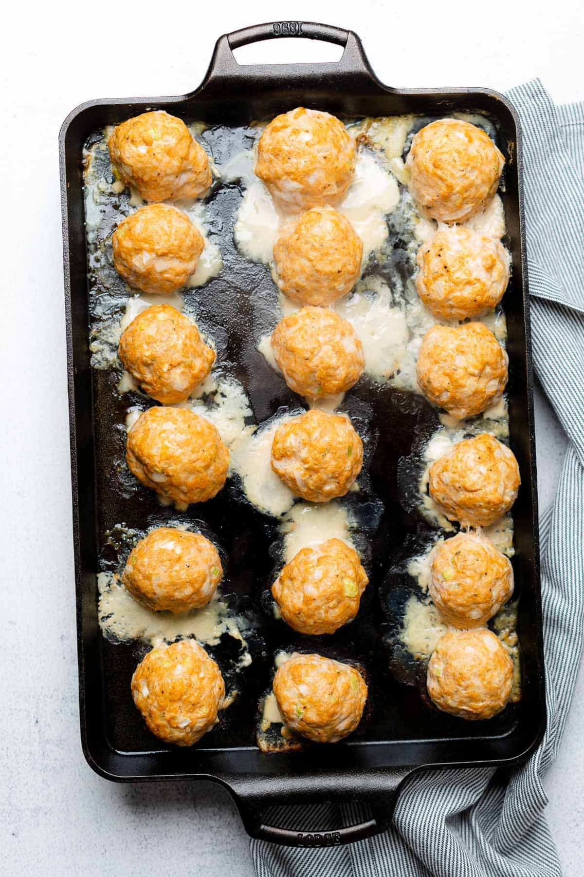 baked turkey meatballs on a bast iron baking sheet with pools of white fat