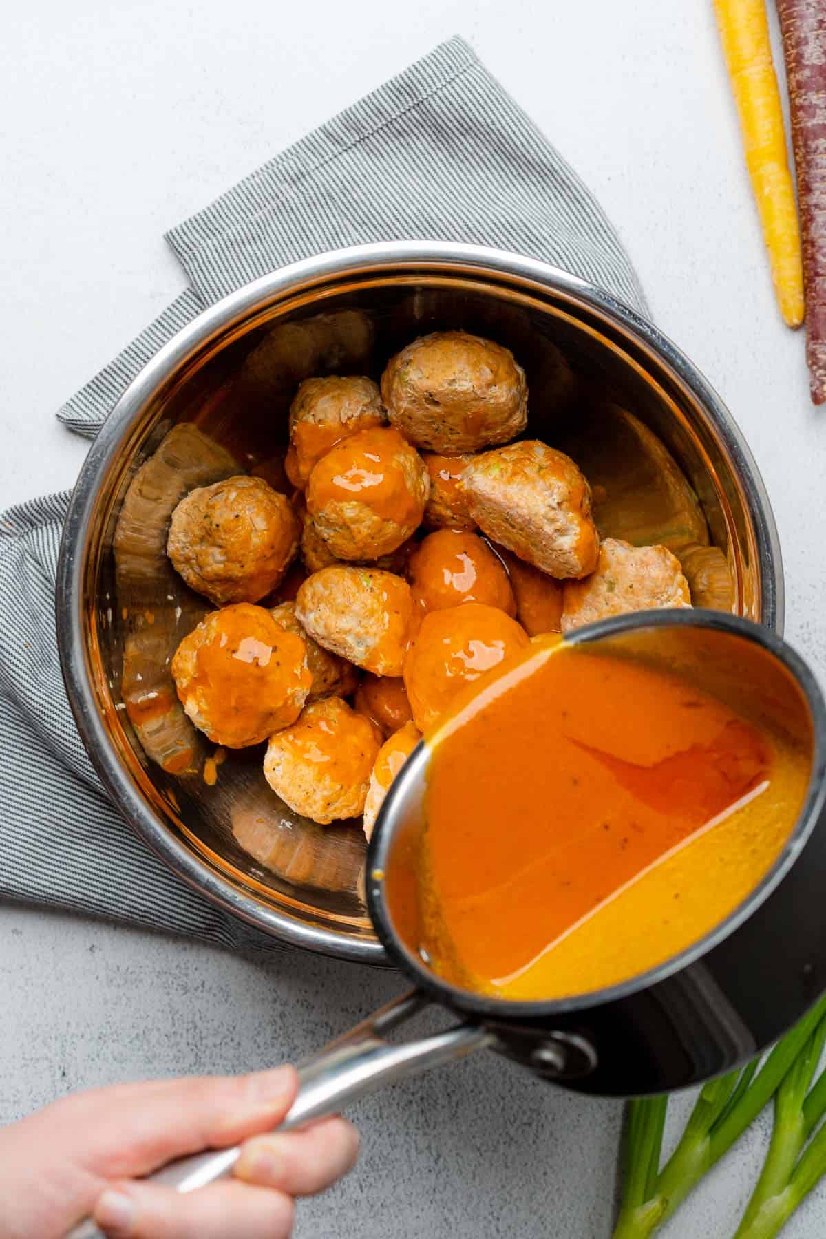 pouring buffalo sauce over top of meatballs in a bowl