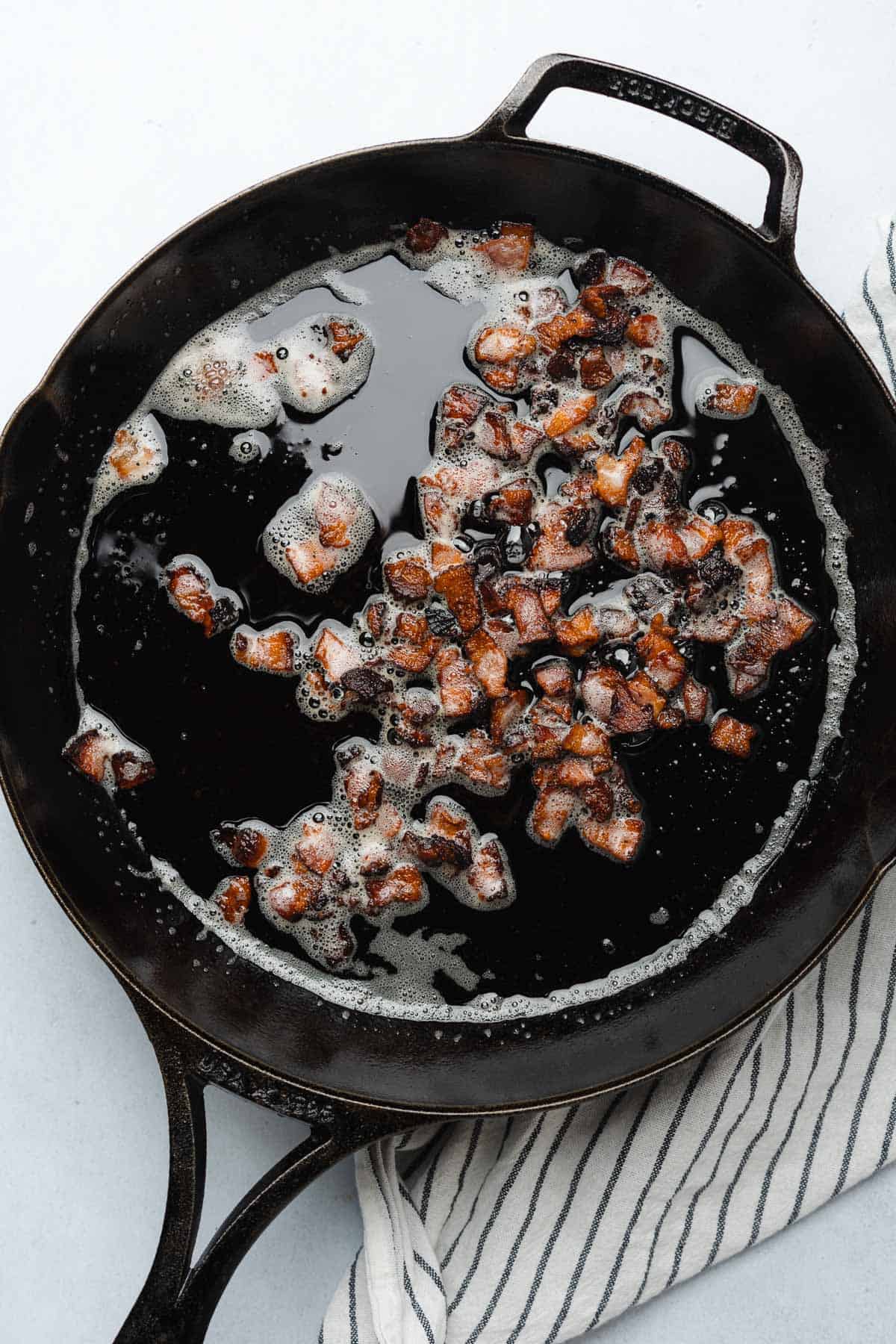 bacon bits cooking in a cast iron skillet