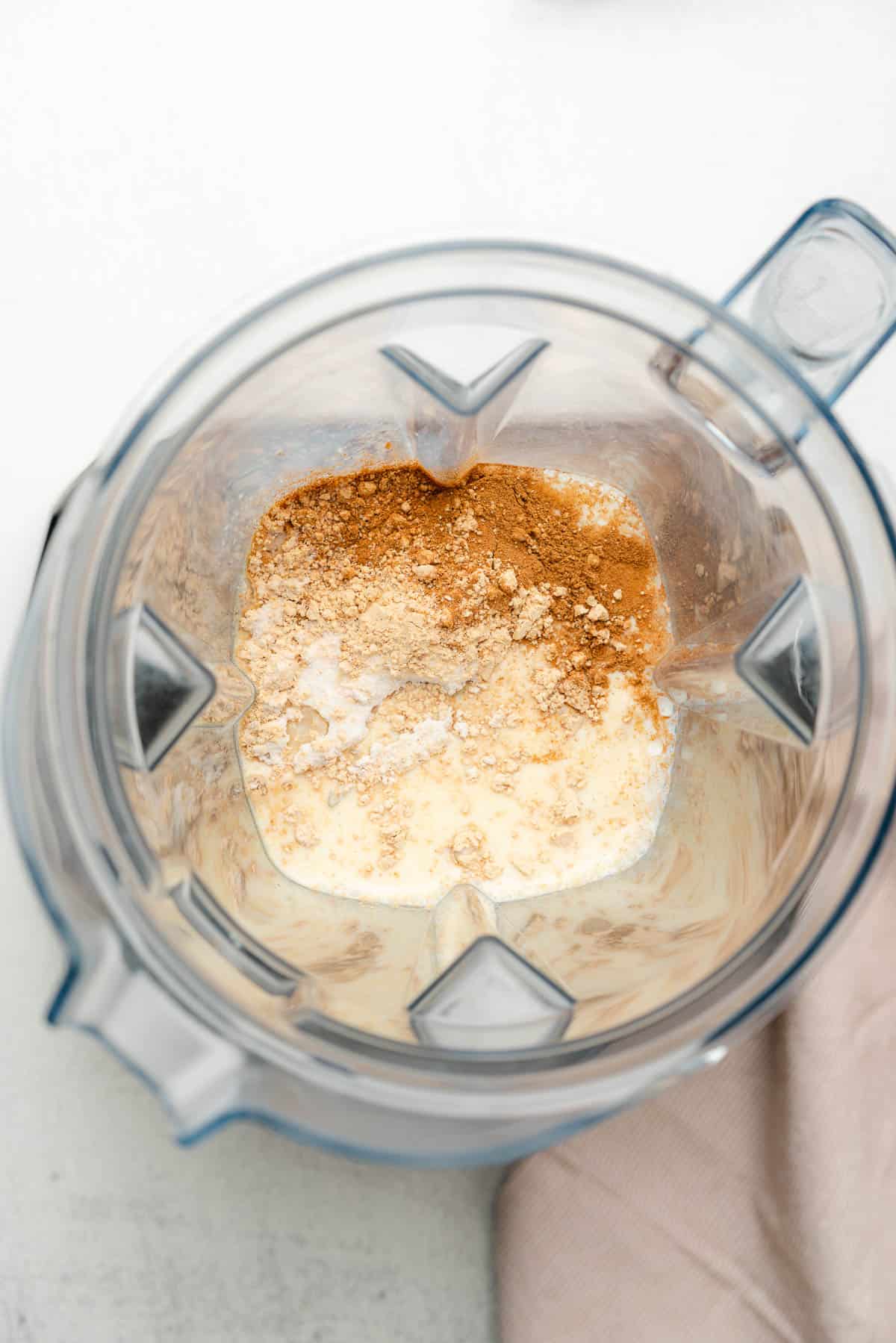 inside of a vitamix blender with milk, peanut butter powder, sweetener, salt and cinnamon inside