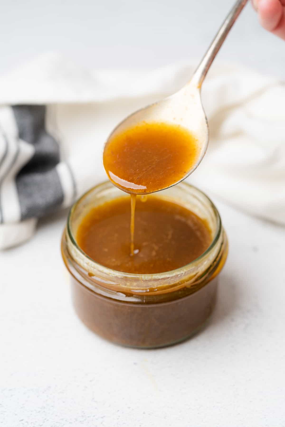 spoonful of homemade creamy balsamic dressing dripping off of a spoon into a jar