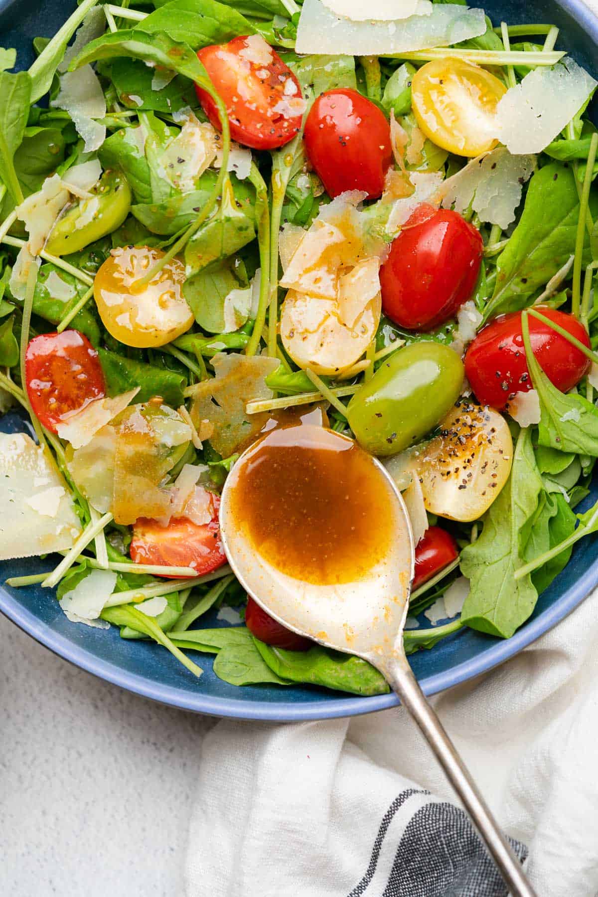 spoonful of creamy balsamic dressing on an arugula side salad with cherry tomatoes