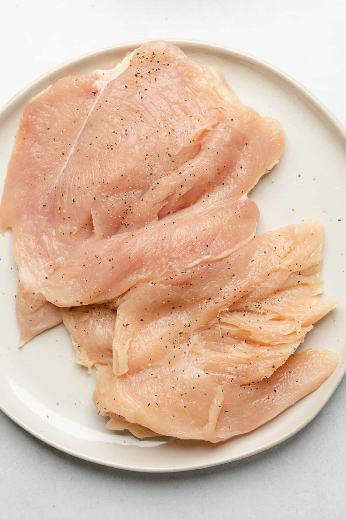 butterflied chicken breasts on a white plate with salt and pepper