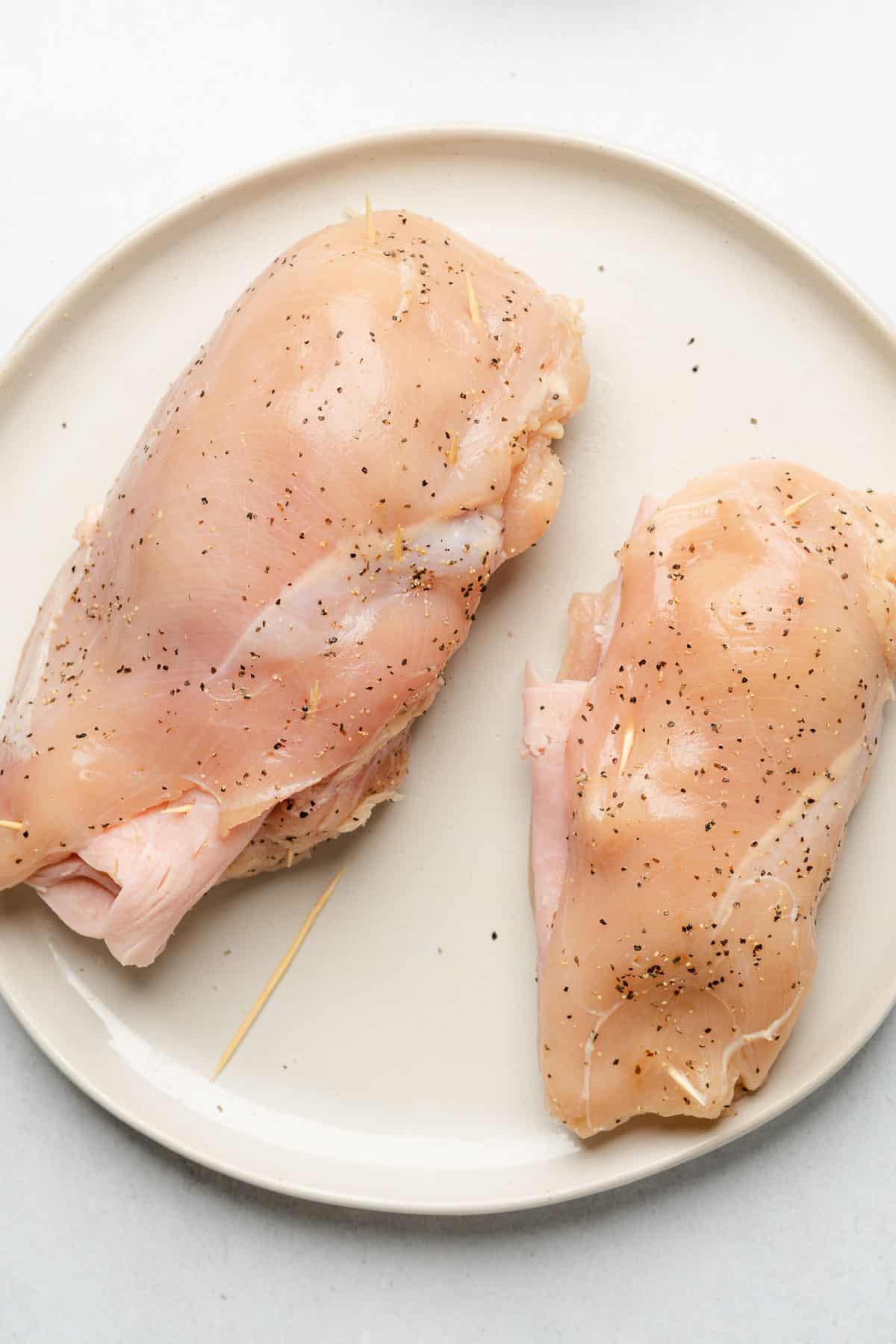 raw chicken breasts on a white plate with salt and pepper filled with ham and swiss cheese then secured with toothpicks