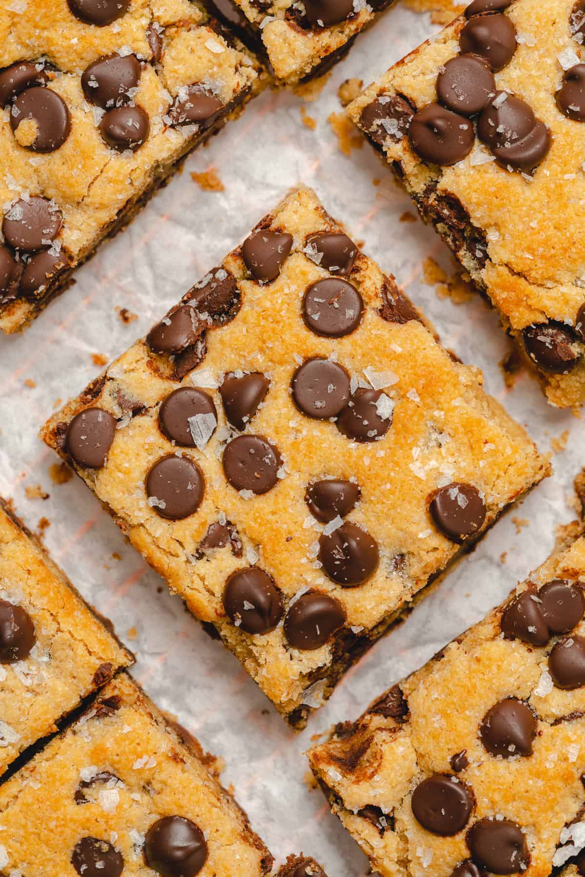 square of a keto chocolate chip cookie bar sprinkled with sea salt surrounded by other cookie bars on parchment paper