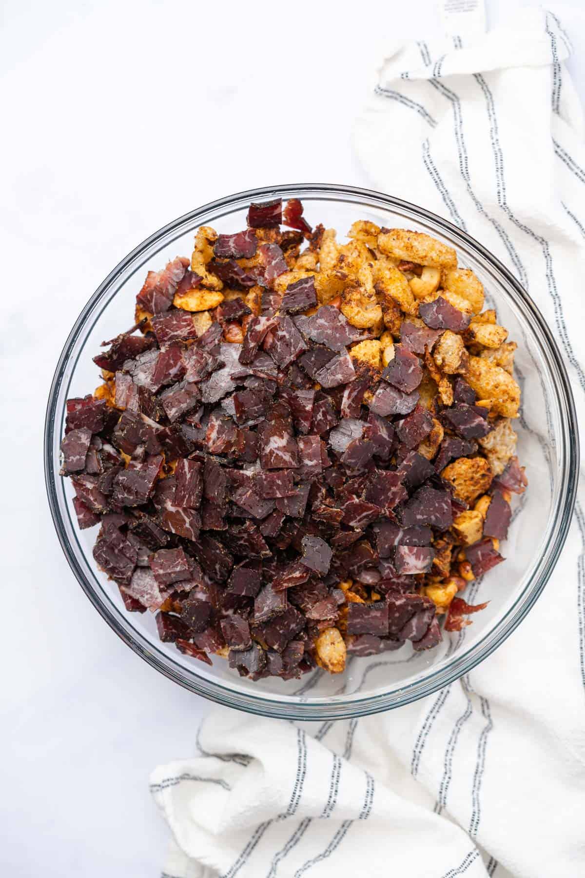 snack mix in a glass bowl with beef biltong on top