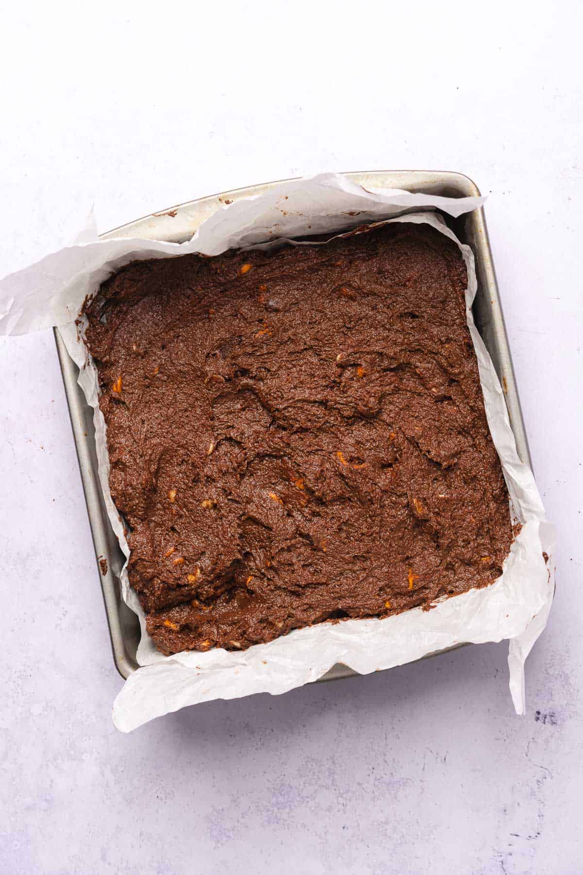 raw brownie batter in a parchment lined baking pan