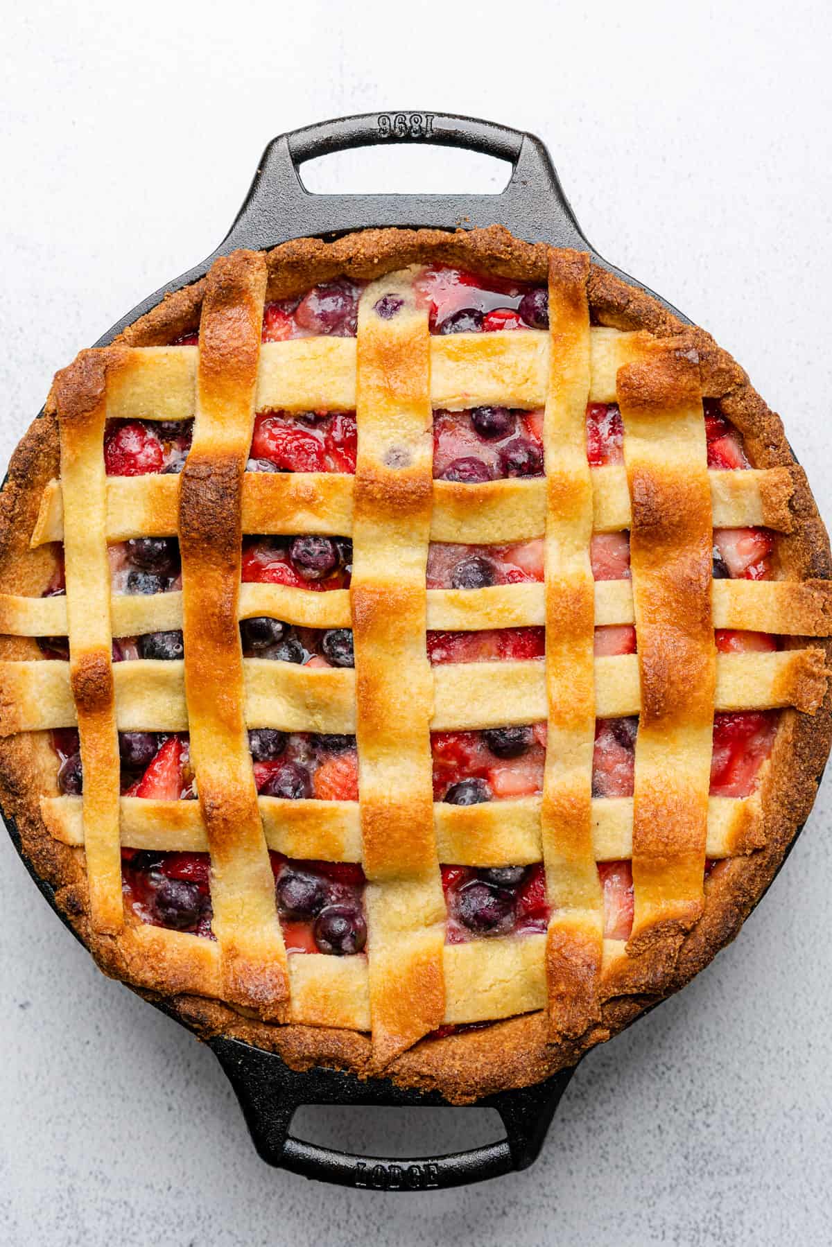 baked strawberry blueberry pie with a lattice design top in a cast iron skillet