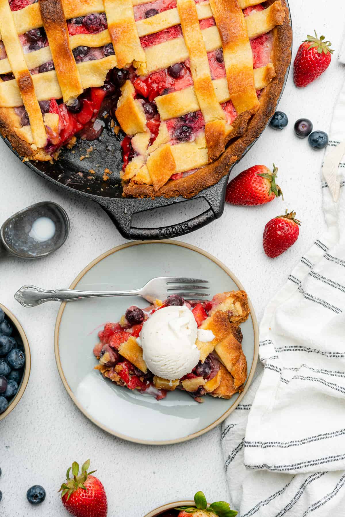 strawberry blueberry pie on a plate with low carb ice cream next to a cast iron skillet with the pie in it