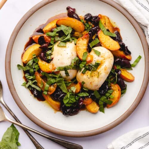 beautiful plate of burrata with baked nectarines and cherries topped with fresh basil