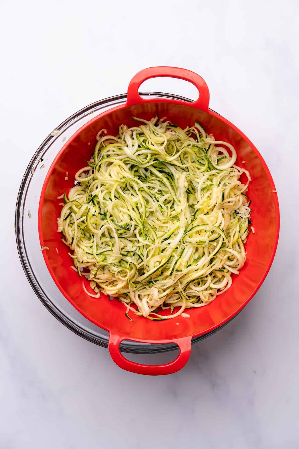 salted zucchini noodles in a red colander to drain out excess moisture 