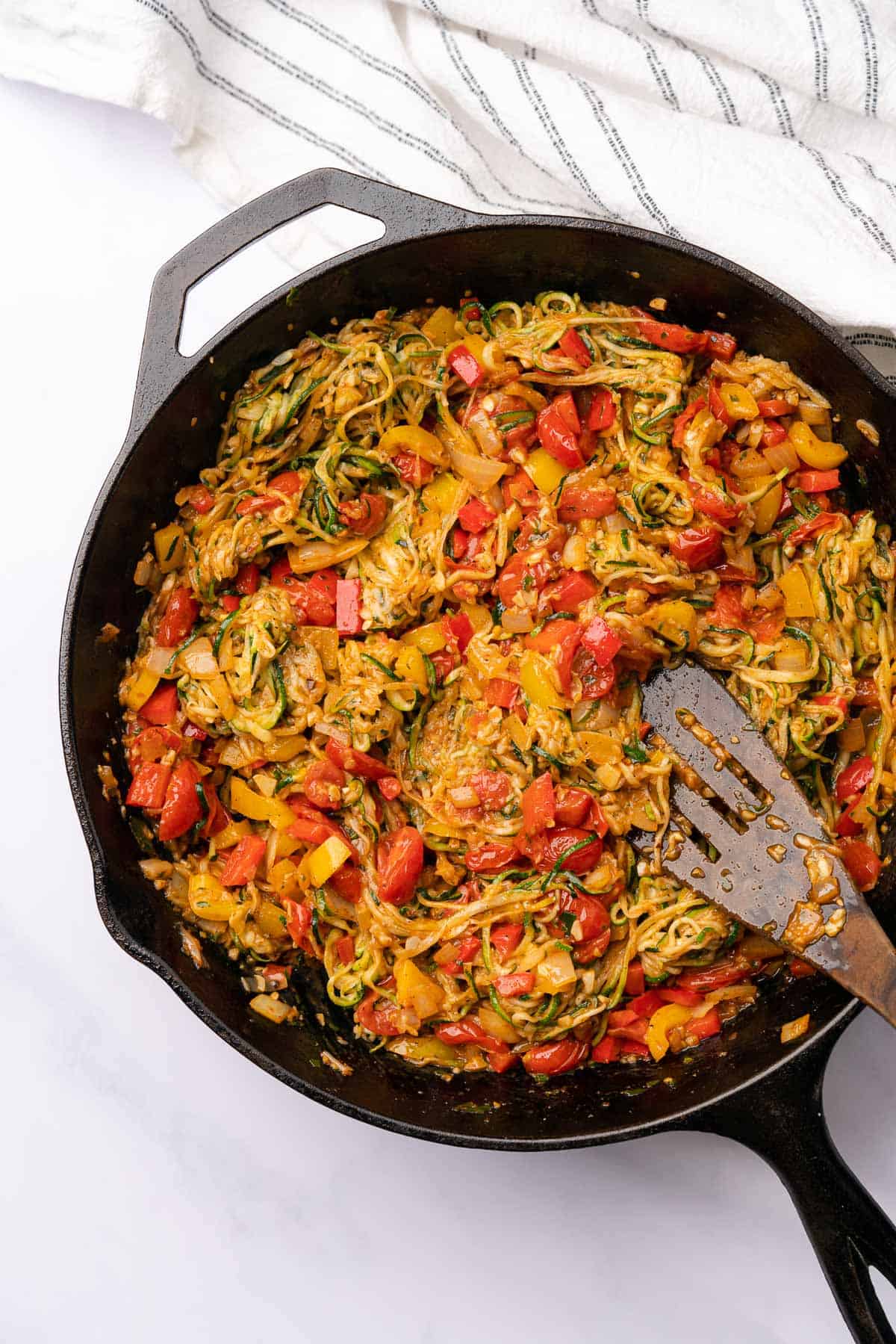 zucchini noodles in a skillet with bell peppers, tomatoes and onions