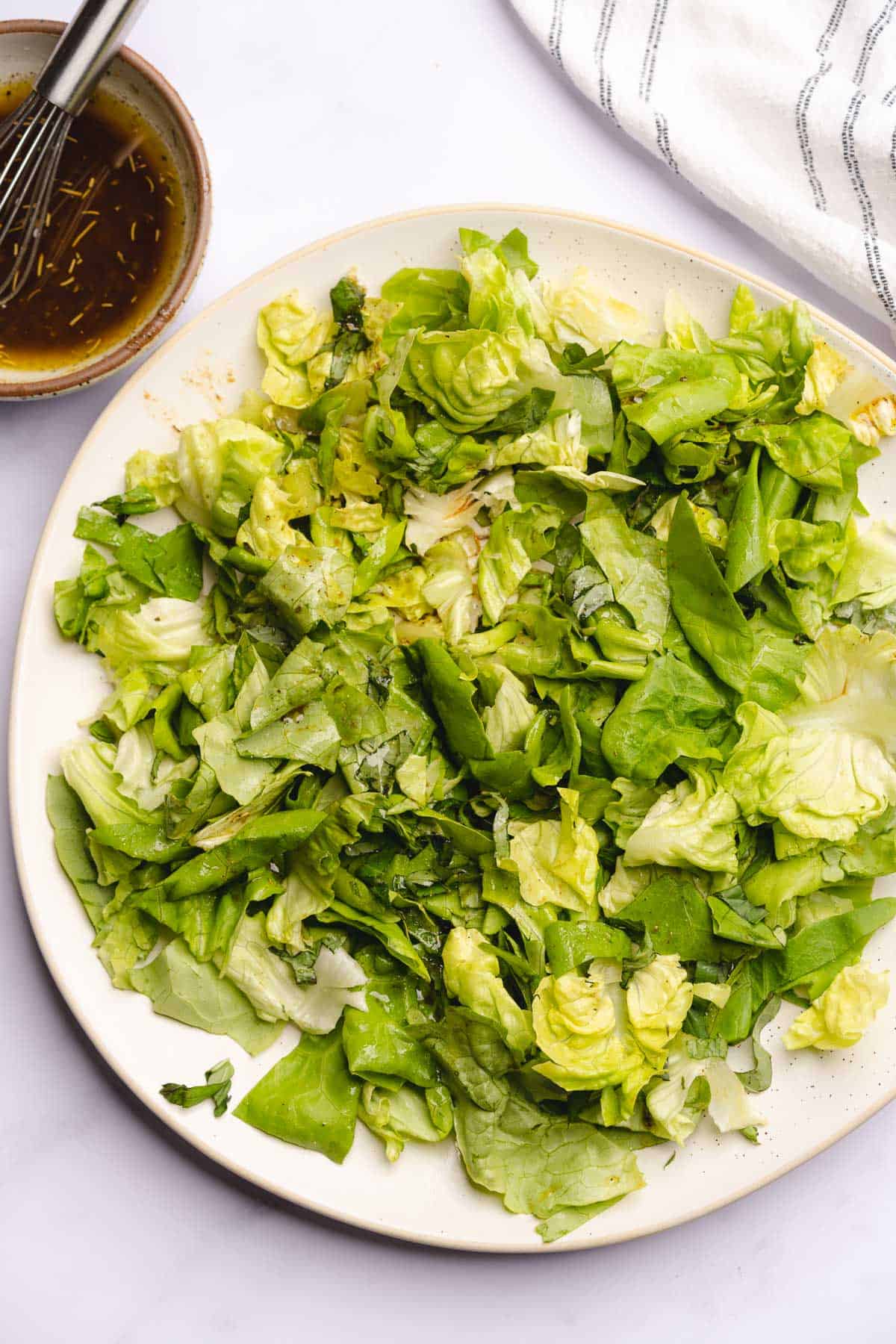 butter lettuce on a large serving platter with basil and salad dressing